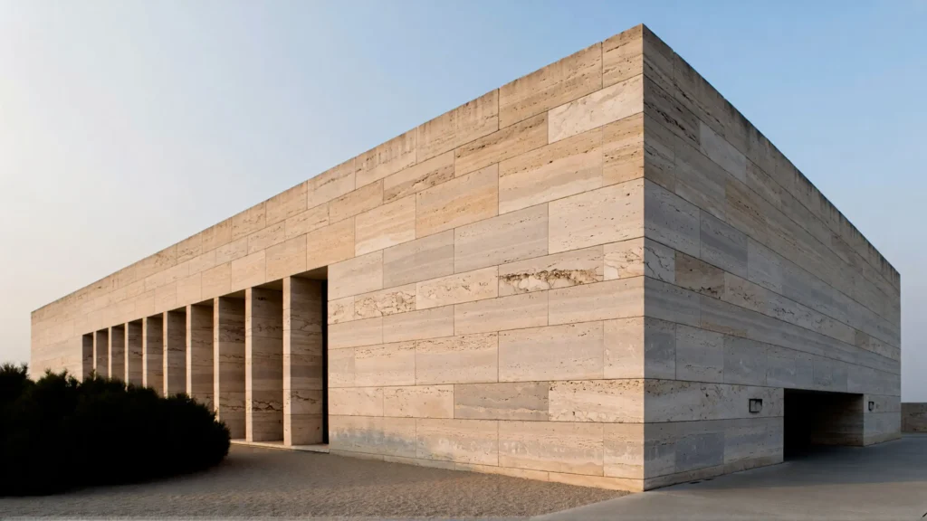 Minimalist building facade clad in natural travertine showcasing texture, aging, and interaction with sunlight