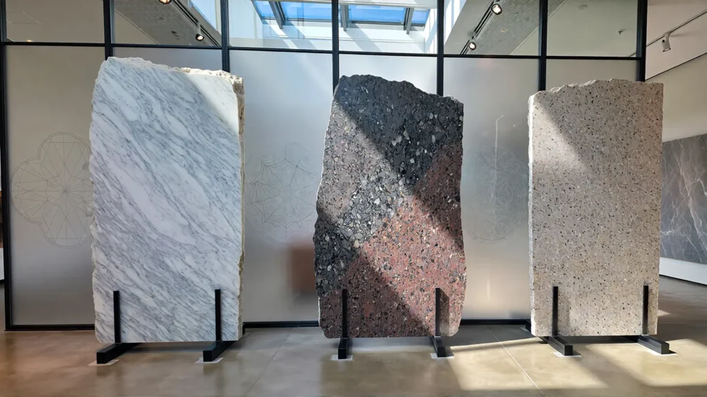 Three natural stone slabs — marble, granite, and quartzite — with subtle geological icons in the background, symbolizing hardness and composition.