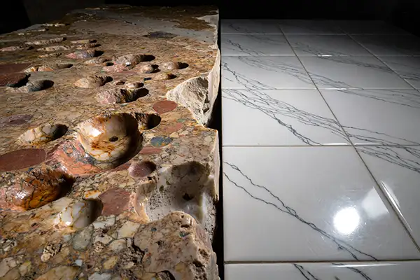 Natural stone slab with organic imperfections contrasted against repeating marble-look porcelain tile pattern
