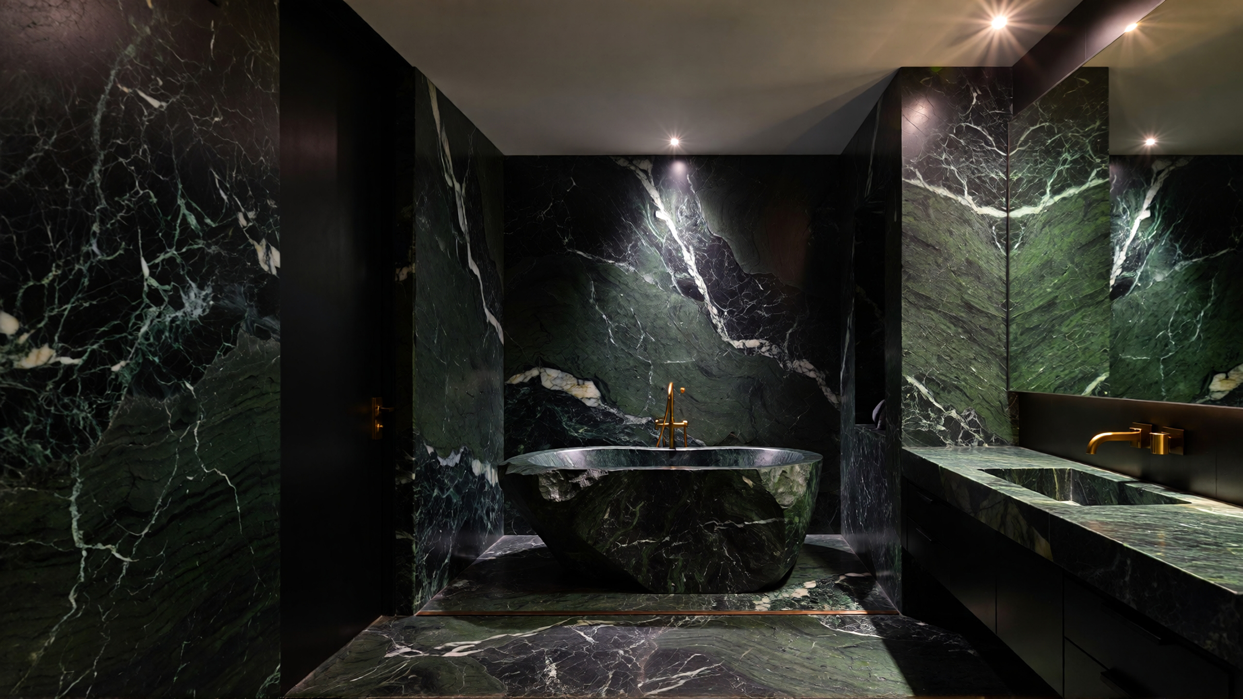 Luxury bathroom designed entirely with Verde Guatemala marble, featuring a sculptural stone bathtub and warm yellow spotlight lighting
